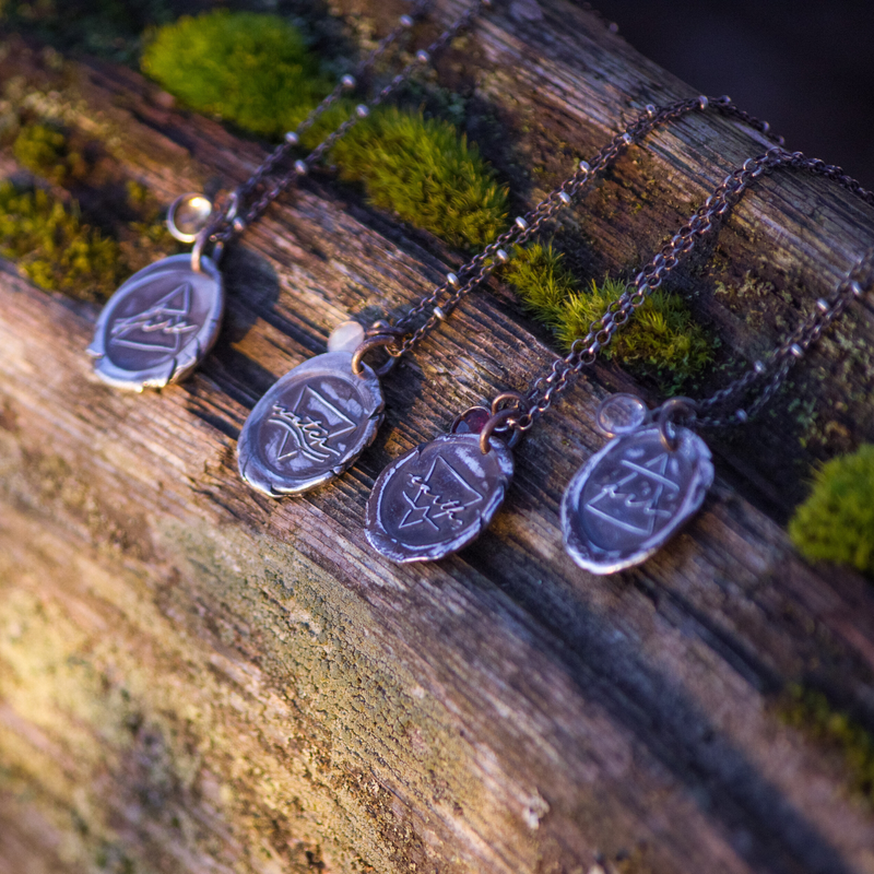 silver wax seal necklaces on mossy background