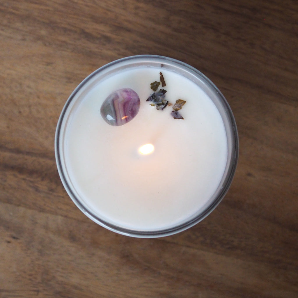 lit top view of gemini zodiac candle with rainbow fluorite crystal and botanicals