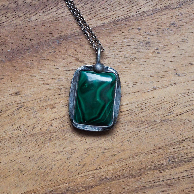 deep green malachite healing crystal talisman necklace on wooden background