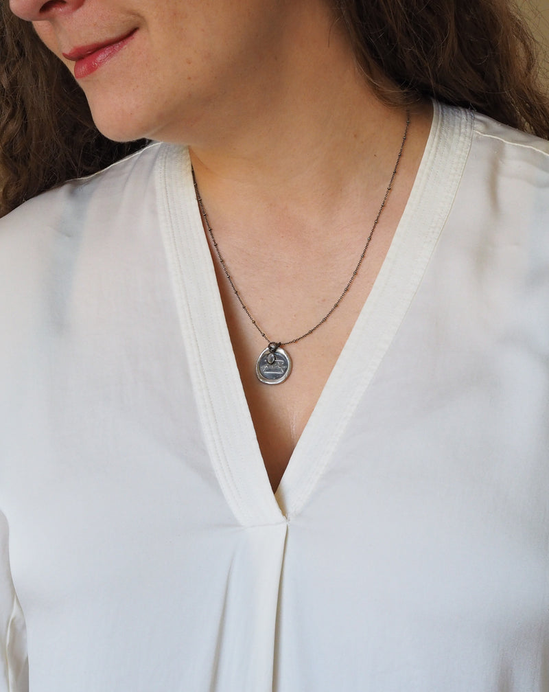 silver air sign talisman necklace on woman in white top