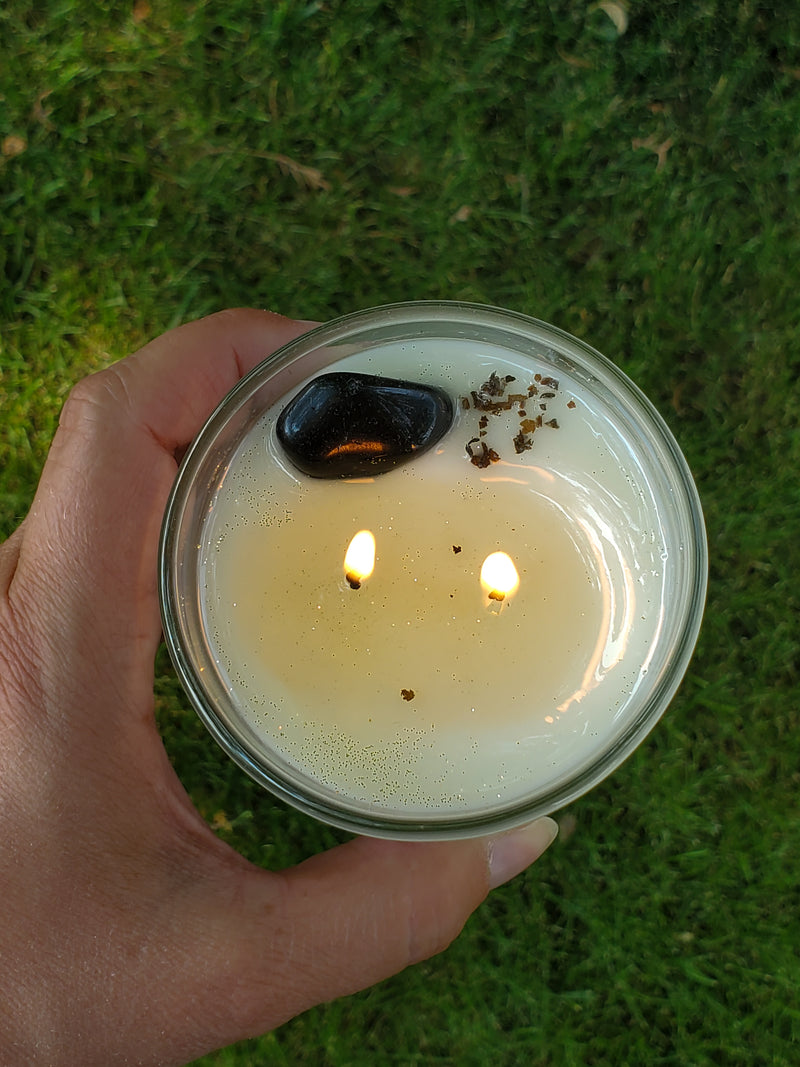 top view of hand holding lit luxury soy candle with black crystal and herbs