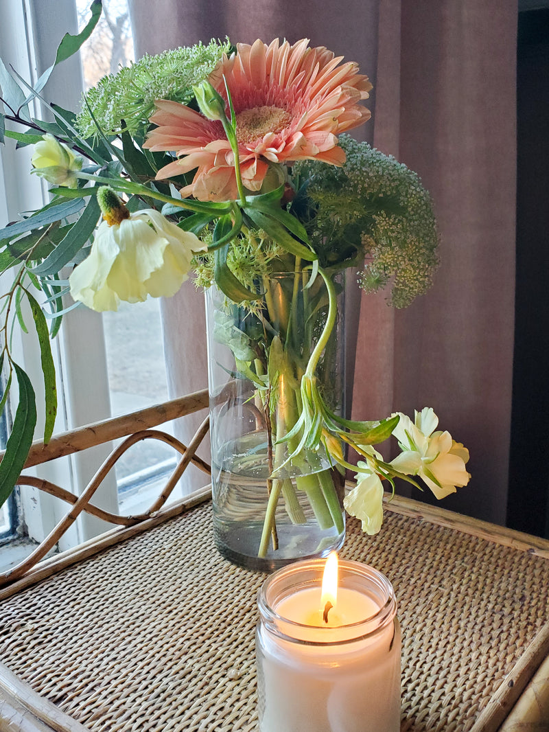 gerbera daisy and fresh greenery with candle on wicker table