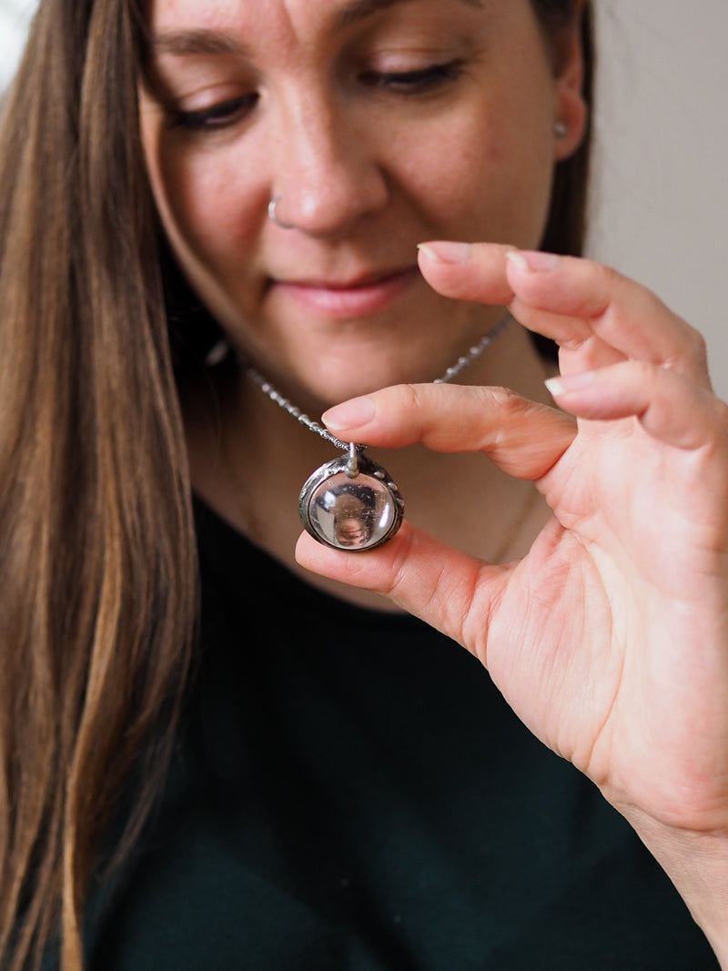 woman holding crystal ball talisman necklace and looking through it