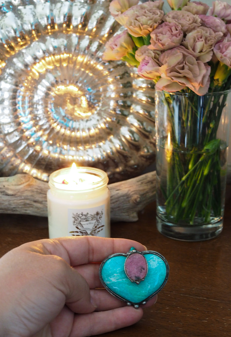 pink and green crystal altar art in palm of hand with candle and cut flowers in the background