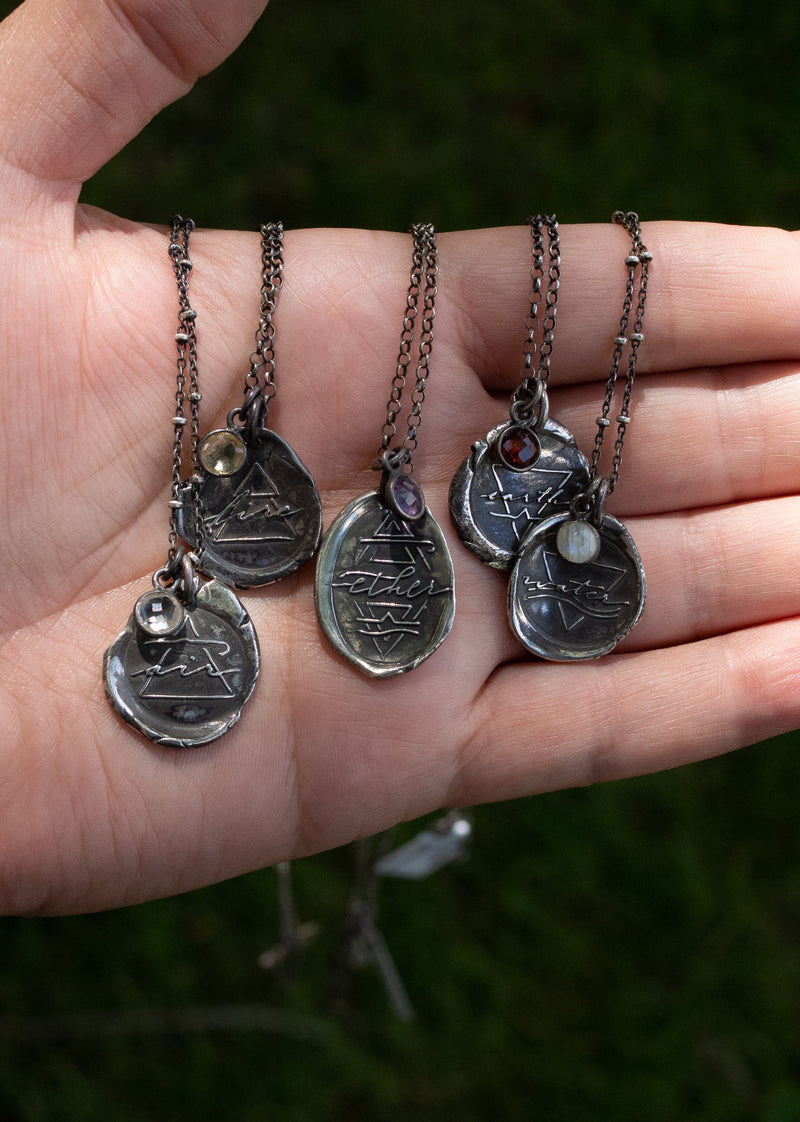 five silver element medallion layering necklaces in palm of hand