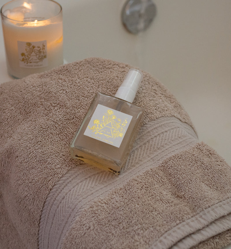 fire ritual mist and botanical soy candle on fluffy towel at edge of bath tub