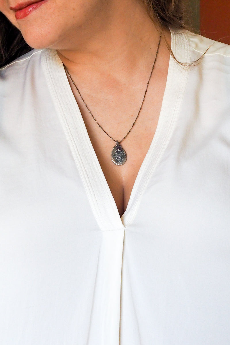 silver medallion necklace with alchemical symbol on woman in white top