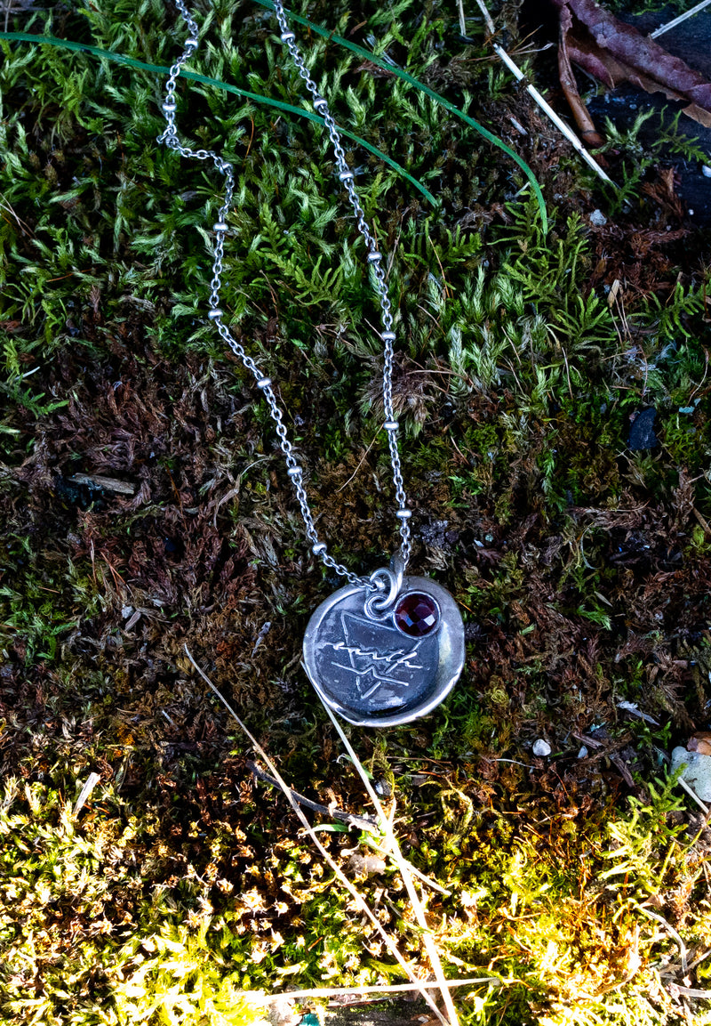 silver earth sign talisman necklace on mossy background