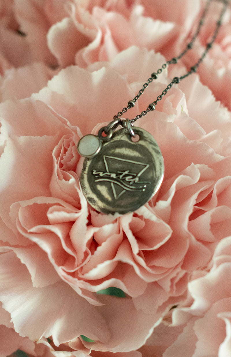 silver water sign element medallion necklace with moonstone on top of pink carnation flower