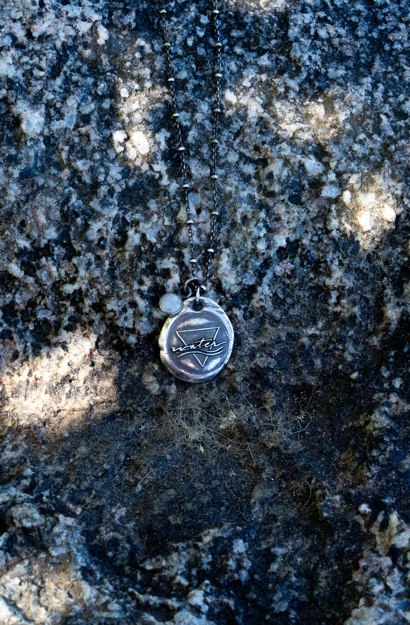 silver water sign necklace on rocky boulder