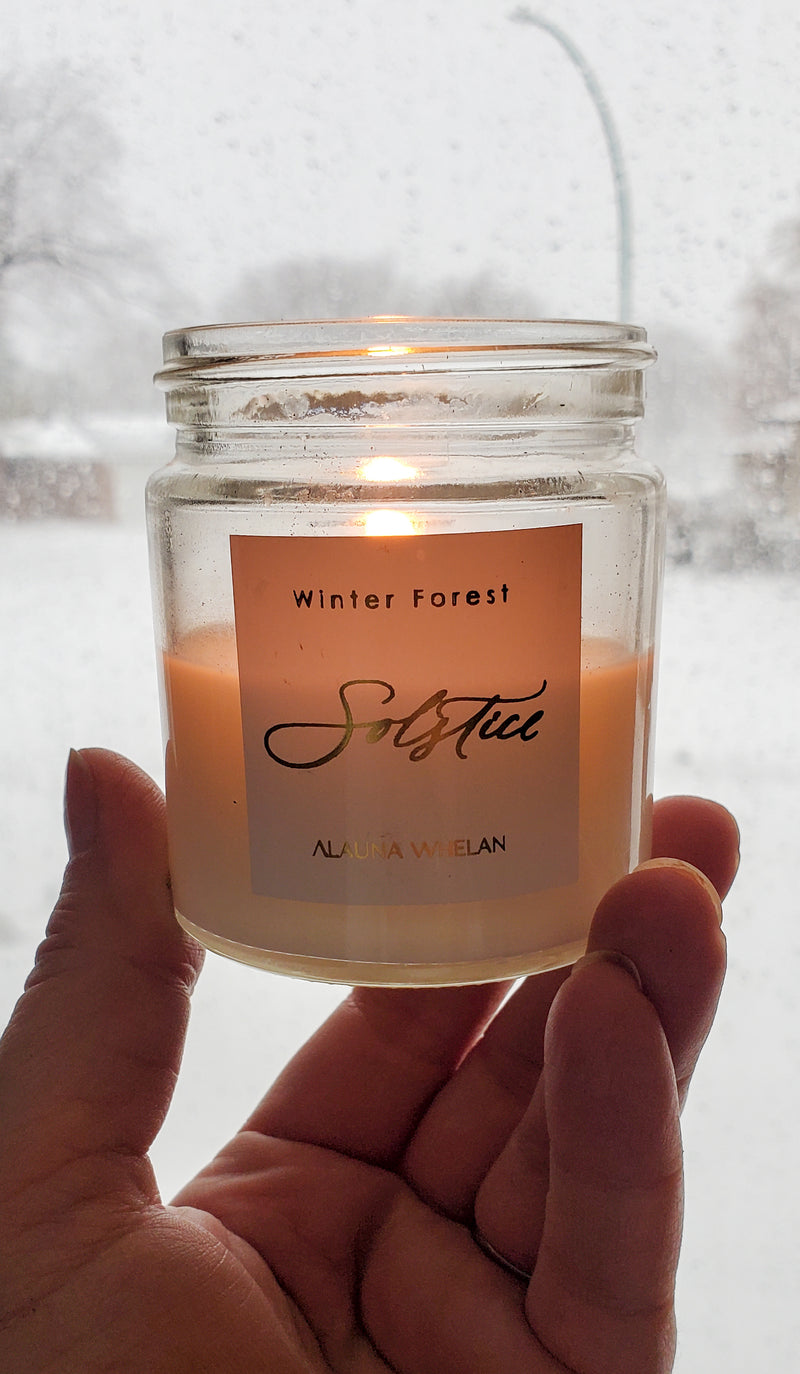 hand holding lit luxury winter solstice soy crystal intention candle with snowy background