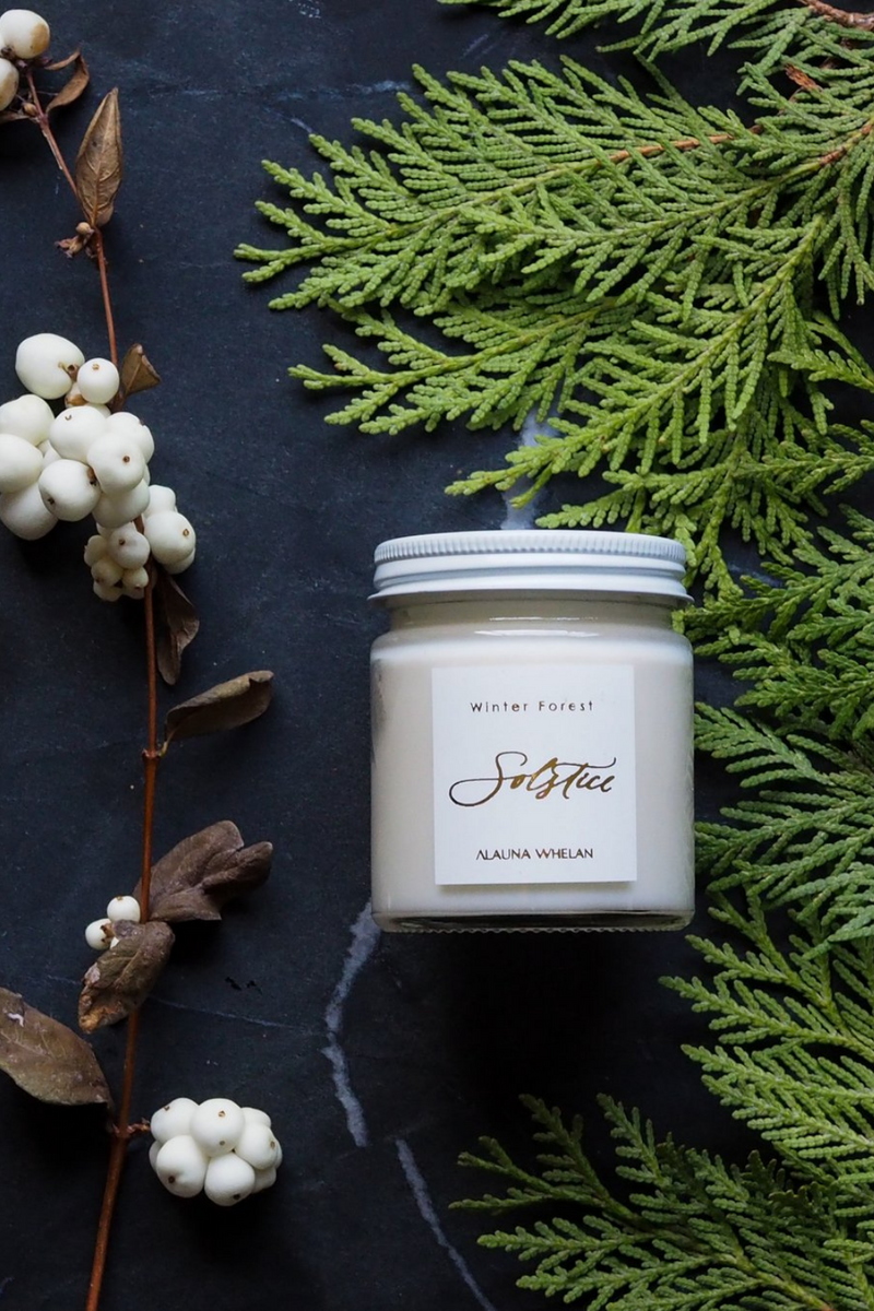 winter solstice soy intention candle on dark background with cedar boughs and branches