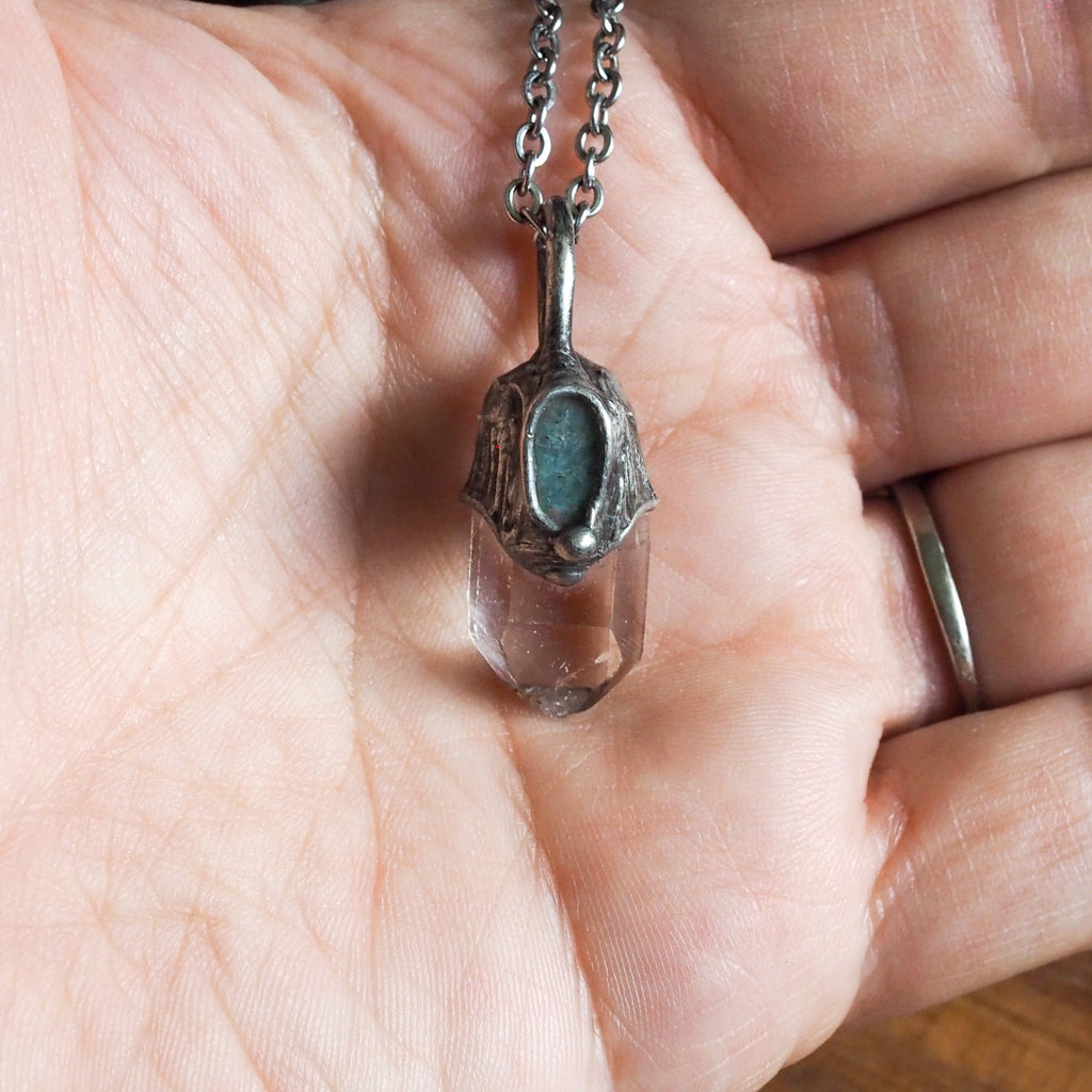 blue and clear healing crystal talisman necklace in palm of hand