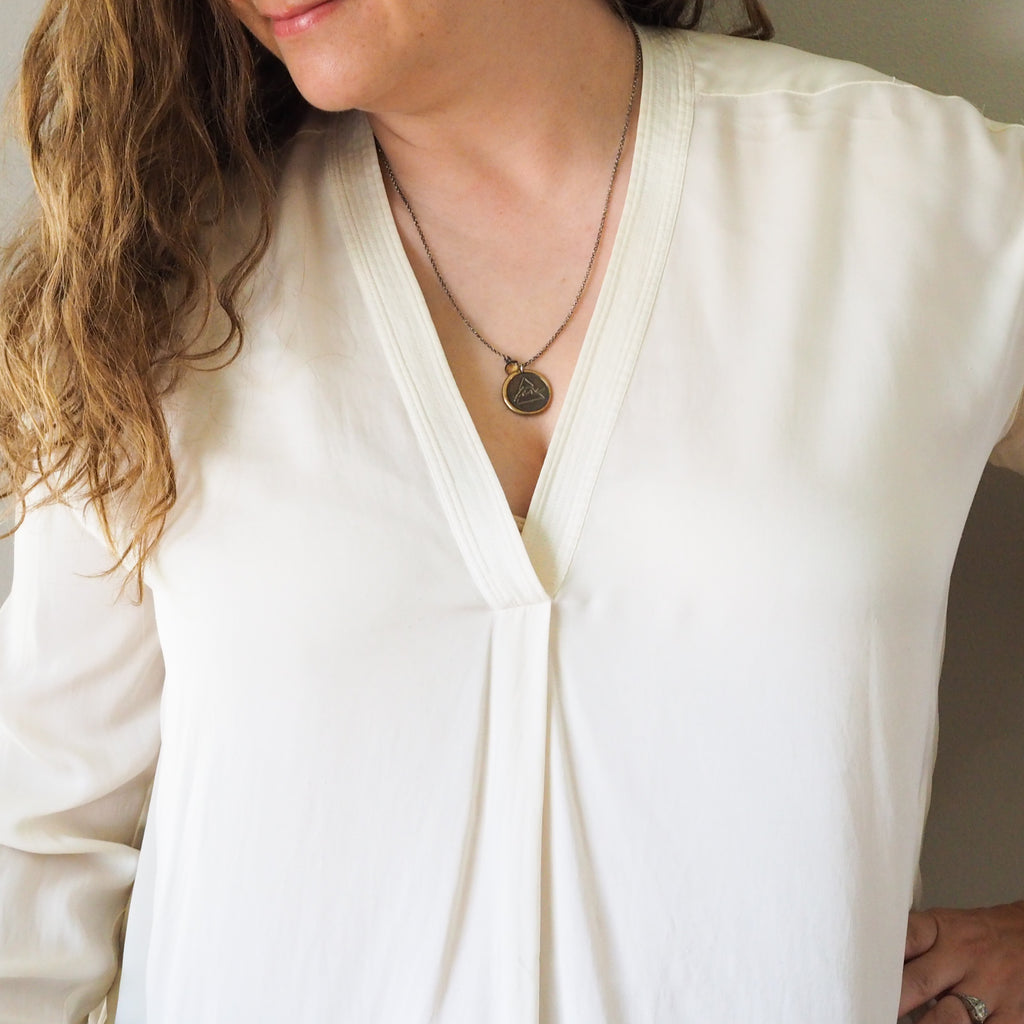 bronze fire element layering talisman necklace on woman in white top