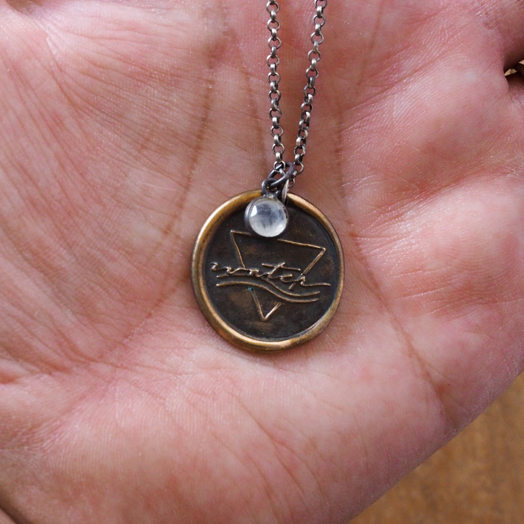 bronze water element layering talisman necklace on palm of hand