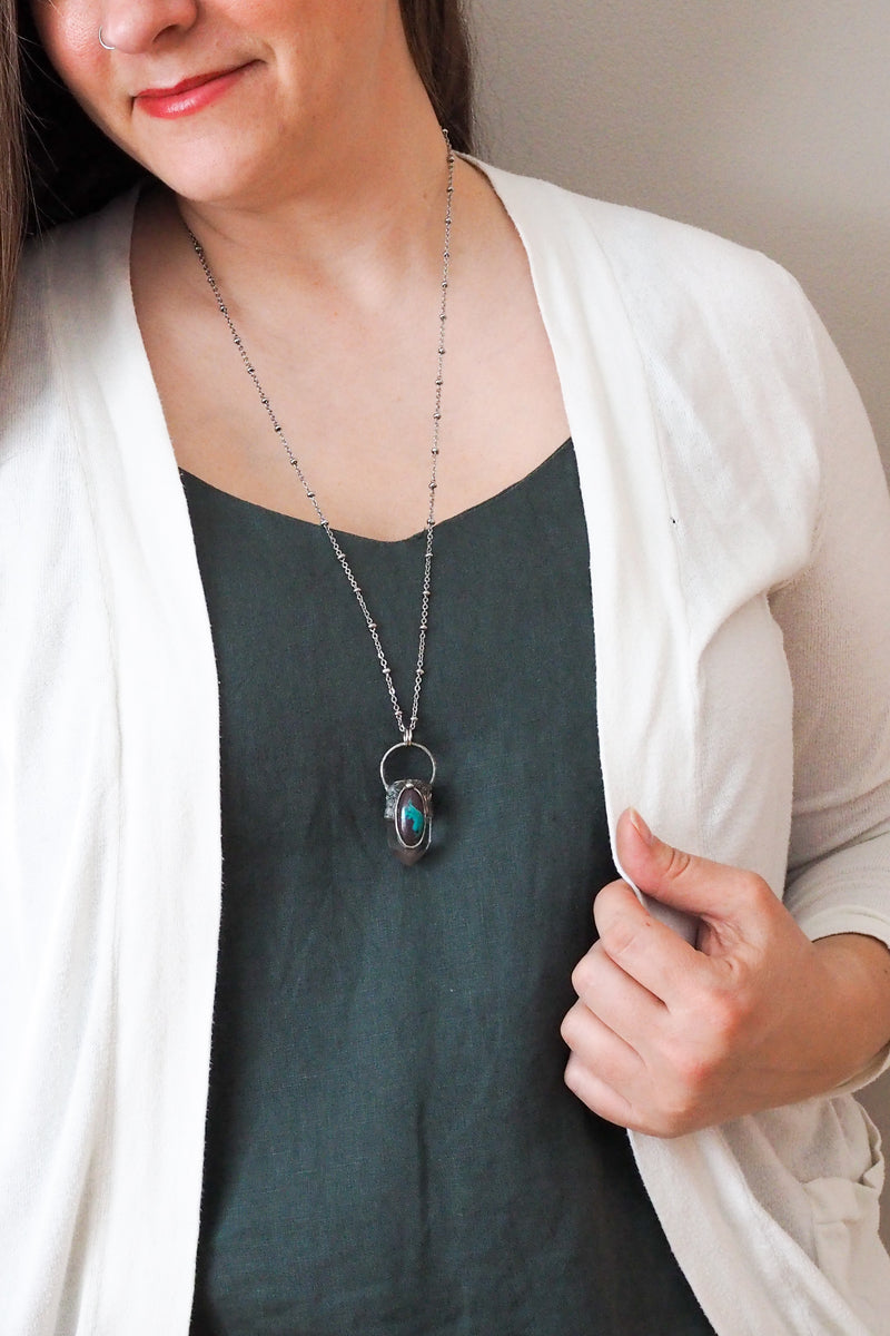brown, blue, and clear gemstone healing crystal talisman statement necklace on woman in blue top with white cardigan