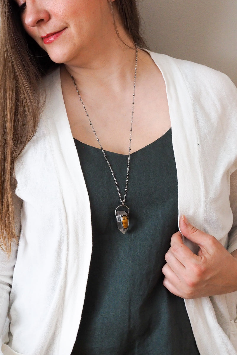 rustic clear and banded yellow healing crystal talisman necklace on woman in blue top with white cardigan