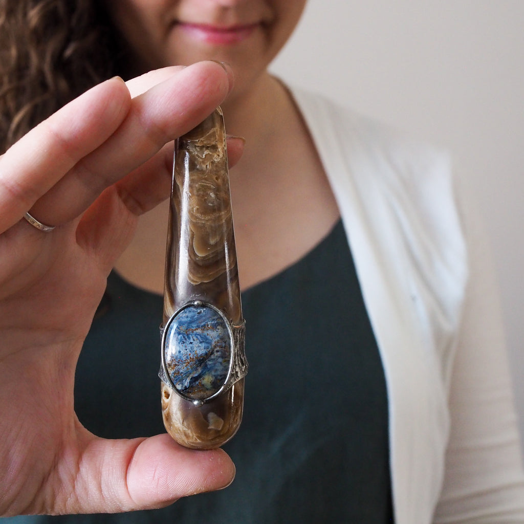 woman holding brown and blue healing crystal talisman wand