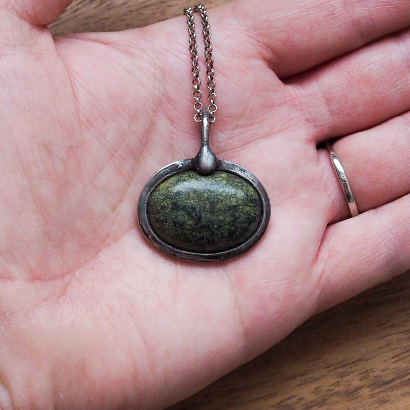 palm of hand holding green healing talisman crystal necklace