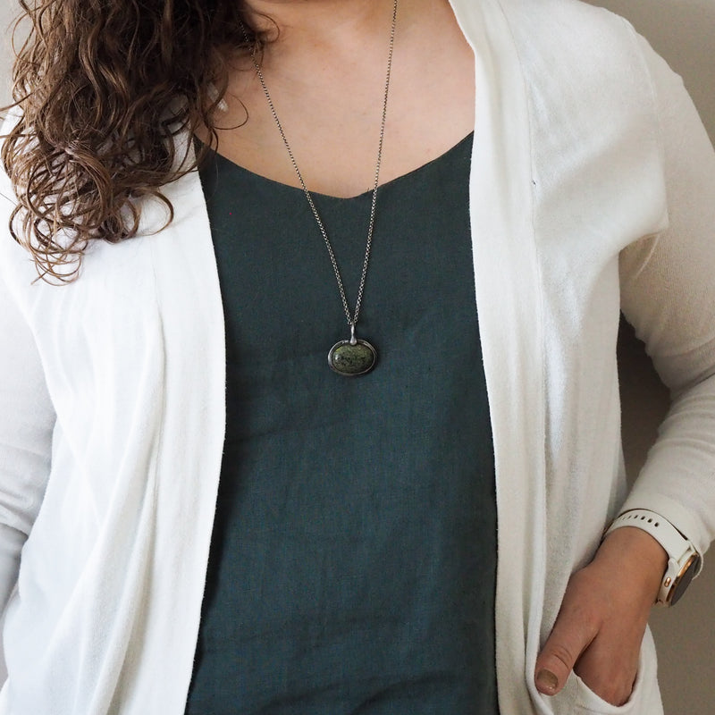 woman in white and blue top wearing green healing talisman crystal necklace