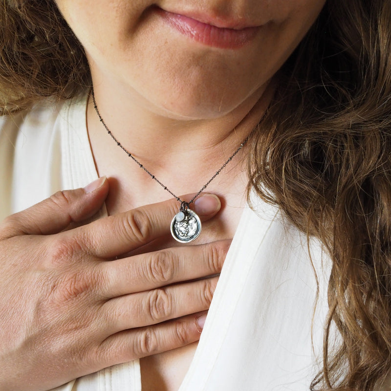 close up of woman in white top wearing a silver full moon lunar talisman layering necklace with rainbow moonstone crystal