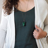 woman in blue and white top wearing deep green malachite healing crystal talisman necklace