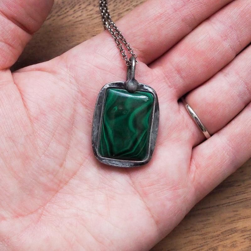 palm of hand holding deep green malachite healing crystal talisman necklace