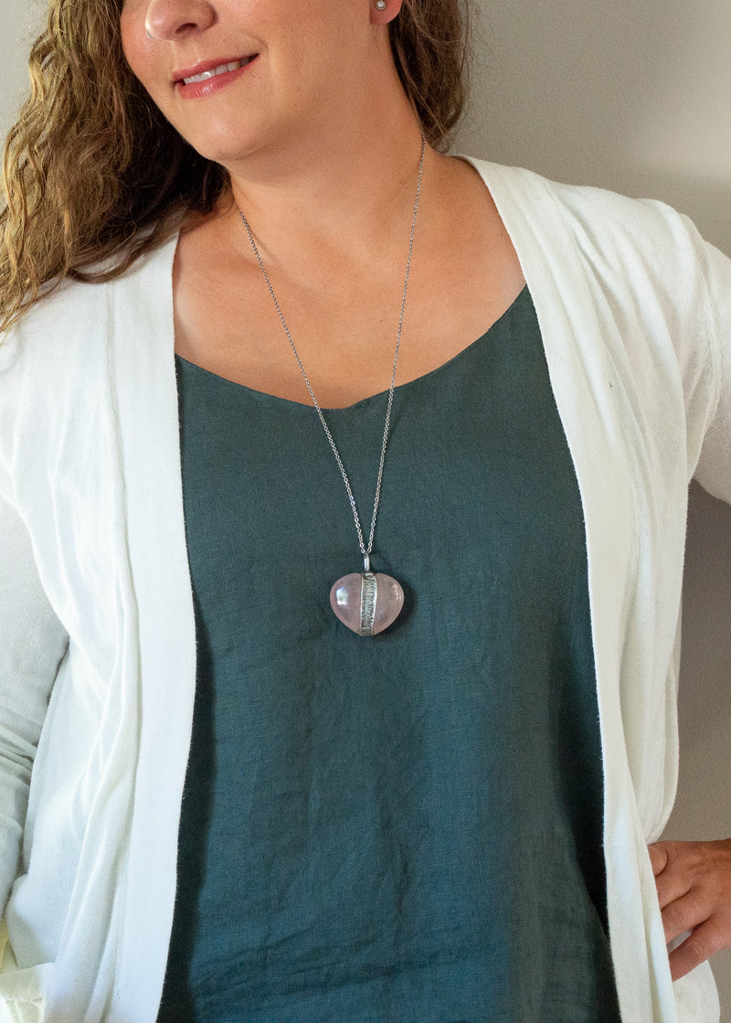 light pink rose quartz heart gemstone talisman necklace on woman with blue top and white cardigan