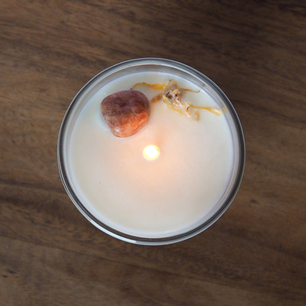 top view of lit leo zodiac candle with orange sunstone crystal and botanicals