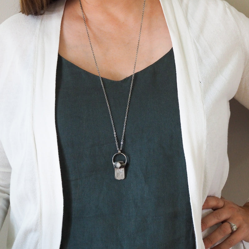 pale pink and white healing crystal talisman necklace on woman in blue top