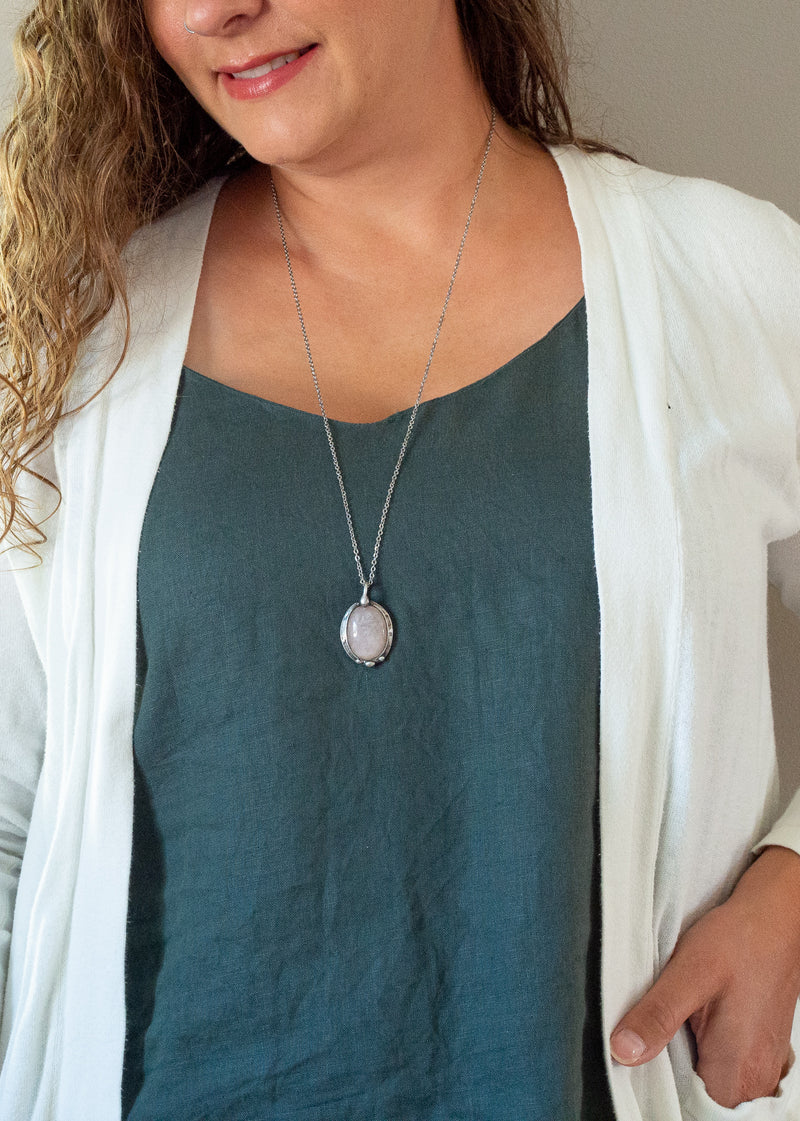 light pink rose quartz gemstone talisman necklace on woman with blue top and white cardigan