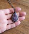 purple crystal talisman necklace on palm of hand