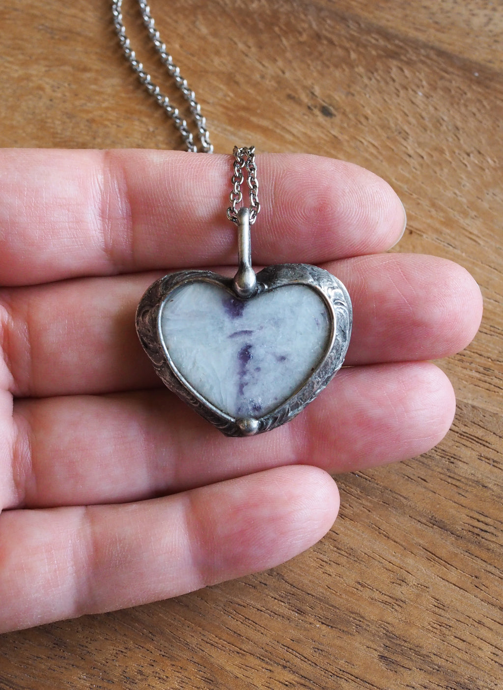 purple and sparkly white heart shaped healing crystal talisman necklace in palm of hand