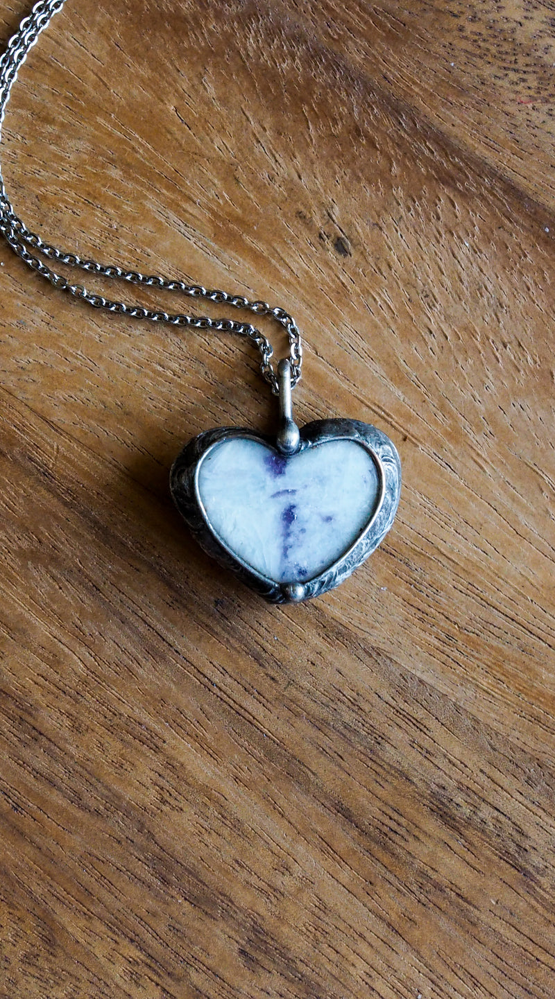 purple and sparkly white heart shaped healing crystal talisman necklace on wooden background