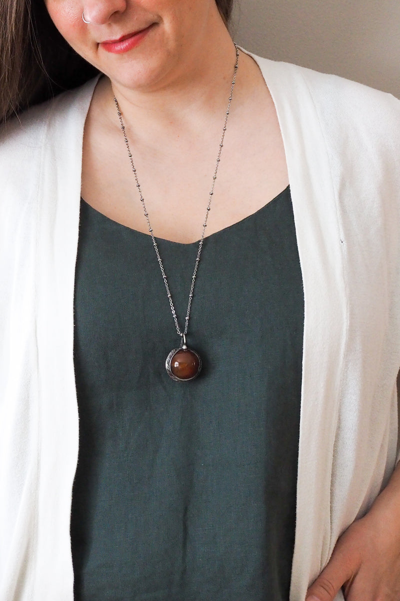 rustic chunky red crystal sphere layering talisman necklace on woman in blue top with white cardigan