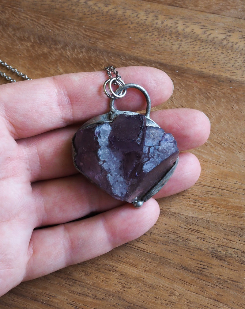 raw purple fluorite crystal talisman necklace in palm of hand