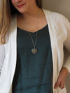 woman in blue top wearing sparkly silver heart shaped healing crystal talisman statement necklace