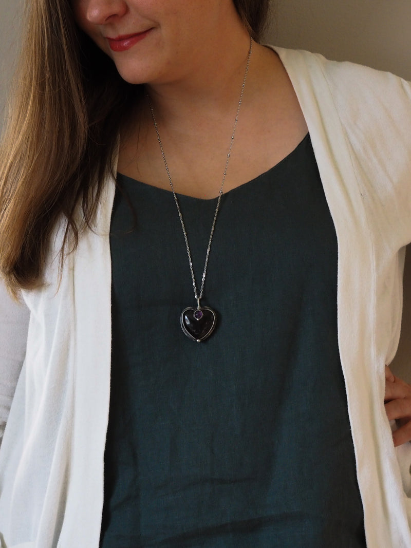 woman in blue top wearing soft grey and purple heart shaped healing crystal talisman statement necklace
