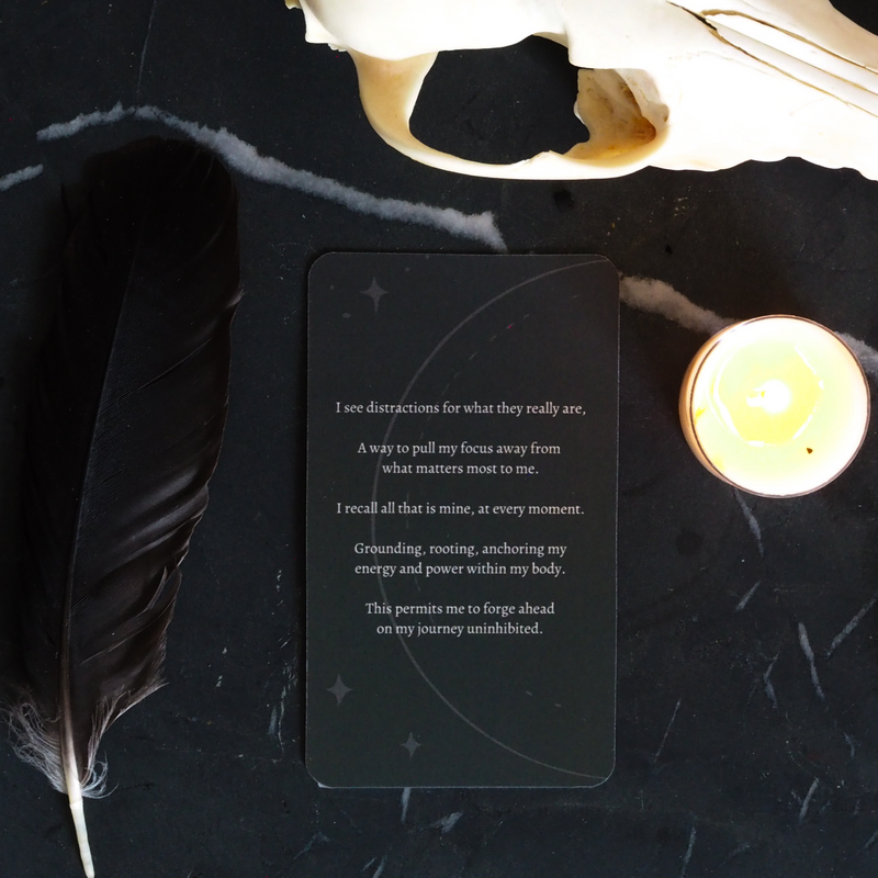 flat lay of moon mantra oracle card on dark background with tealight, feather, and skull