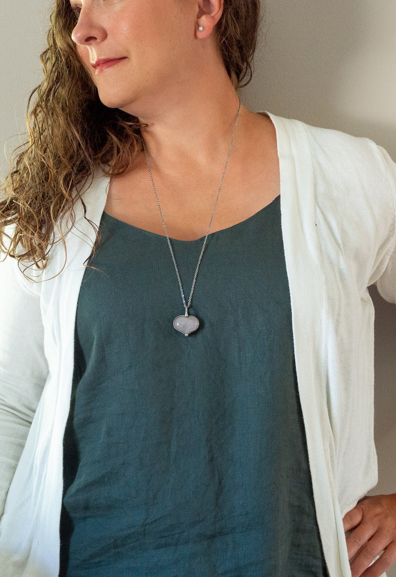 light pink rose quartz heart gemstone talisman necklace on woman with blue top and white cardigan