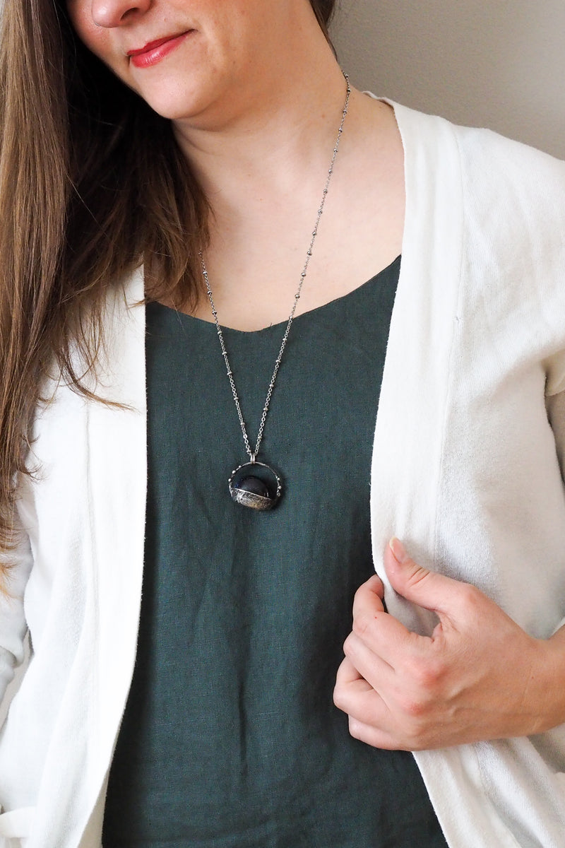 dark blue sparkly crystal talisman necklace on woman in blue top with white sweater
