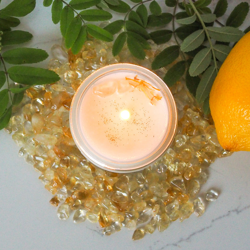 top view of lit summer solstice soy crystal intention candle with greenery, citrus fruit, and crystals