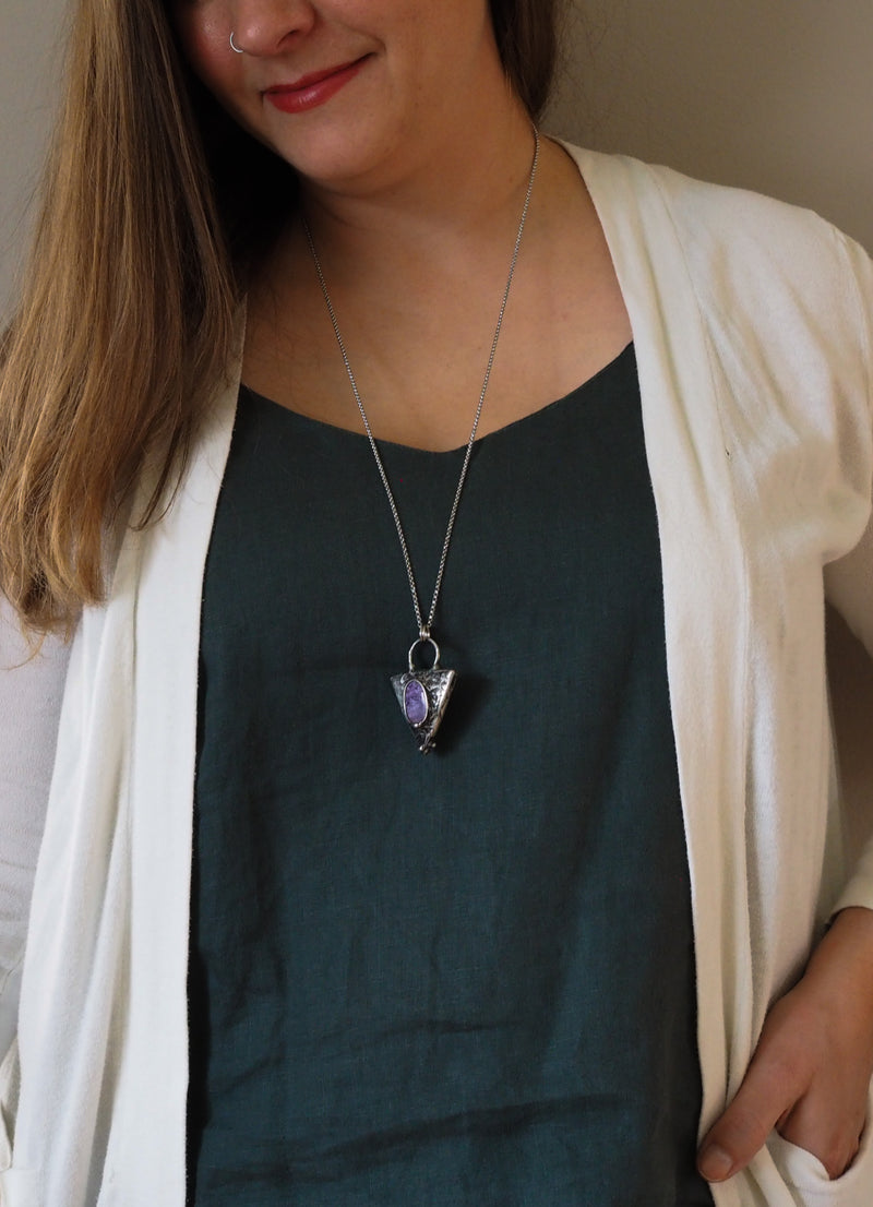 woman in blue top wearing purple gemstone triangle crystal talisman statement necklace